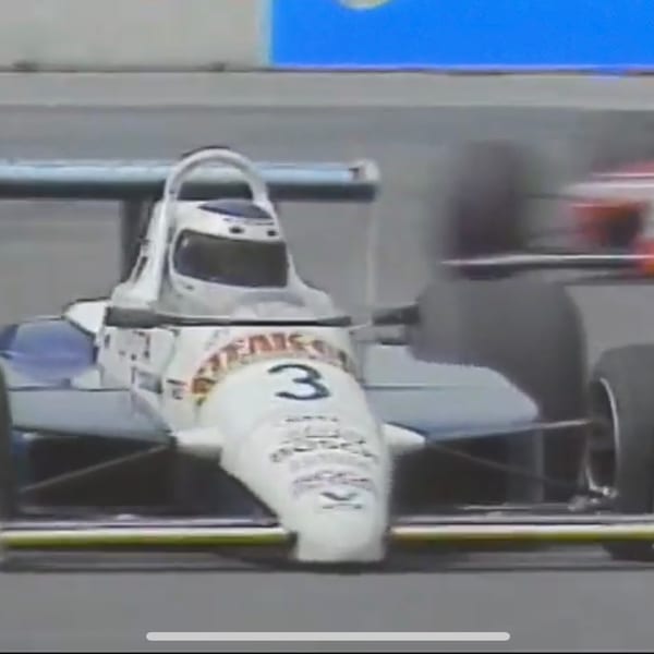 A white and blue race car with the number 3 on its nose speeds around a track.