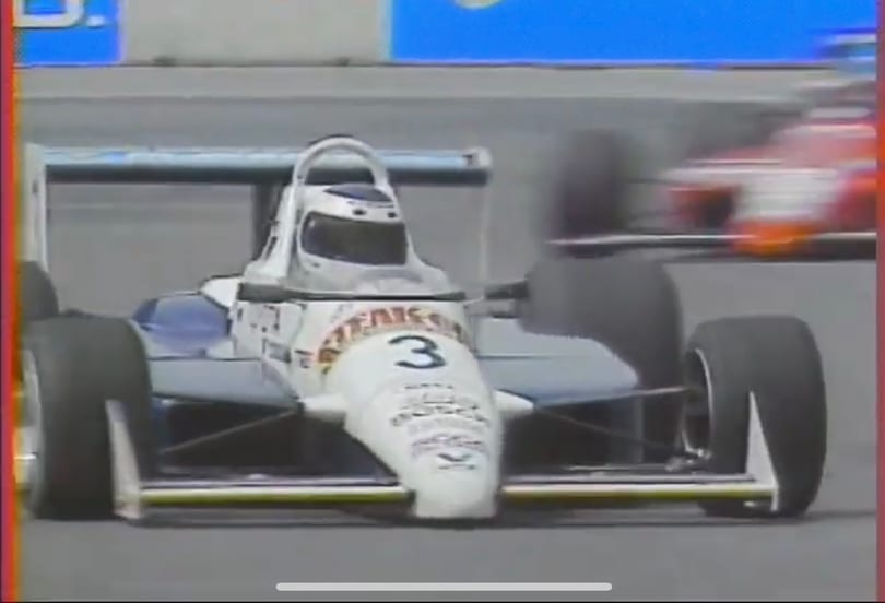 A white and blue race car with the number 3 on its nose speeds around a track.