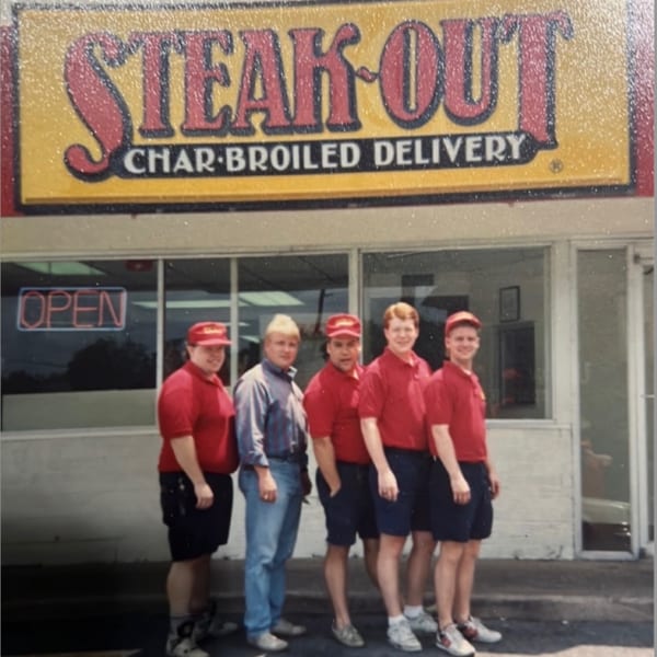 Five young men, four in red uniforms, stand outside a Steak-Out Char-Broiled Delivery restaurant.